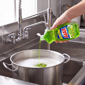 Ajax Lime and Vinegar dish liquid being poured from the 12.4 oz. bottle into a stainless steel stock pot in a commercial sink