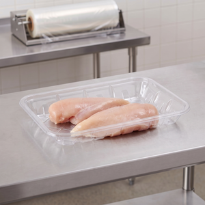 CKF 86601 #2 clear PET plastic meat tray holding two raw boneless chicken breasts on a stainless steel table in a meat packing room