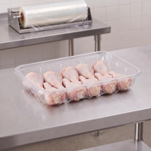 CKF 86631 #42P clear PET plastic meat tray holding raw chicken drumsticks on a stainless steel table in a meat packing room