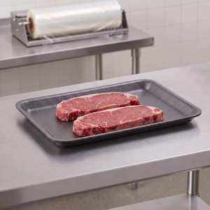 CKF 87834 #4S black foam meat tray holding two raw beef sirloin steaks on a stainless steel table in a meat packing room