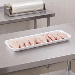 CKF 88107 #7H white foam meat tray holding a row of raw chicken wings on a stainless steel table in a meat packing room