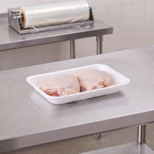 CKF 88111 #2PP white foam meat tray holding two raw bone-in chicken thighs on a stainless steel table in a meat packing room