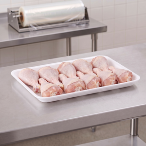 CKF 88140 #1216 white foam meat tray holding raw chicken drumsticks on a stainless steel table in a meat packing room