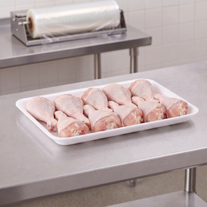 CKF 88141 #10K white foam meat tray holding raw chicken drumsticks on a stainless steel table in a meat packing room