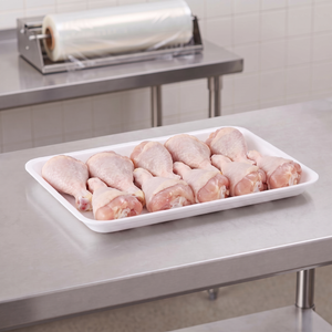 CKF 88144 #8P white foam meat tray holding raw chicken drumsticks on a stainless steel table in a meat packing room