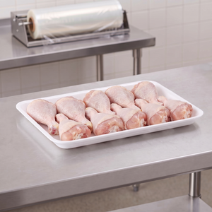 CKF 88156 #15P white foam meat tray holding a row of raw chicken drumsticks on a stainless steel table in a meat packing room