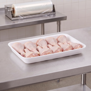 CKF 88157 #25D white foam meat tray holding raw chicken drumsticks on a stainless steel table in a meat packing room