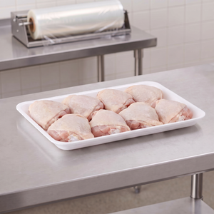 CKF 88176 #4PR white foam meat tray holding raw bone-in chicken thighs on a stainless steel table in a meat packing room